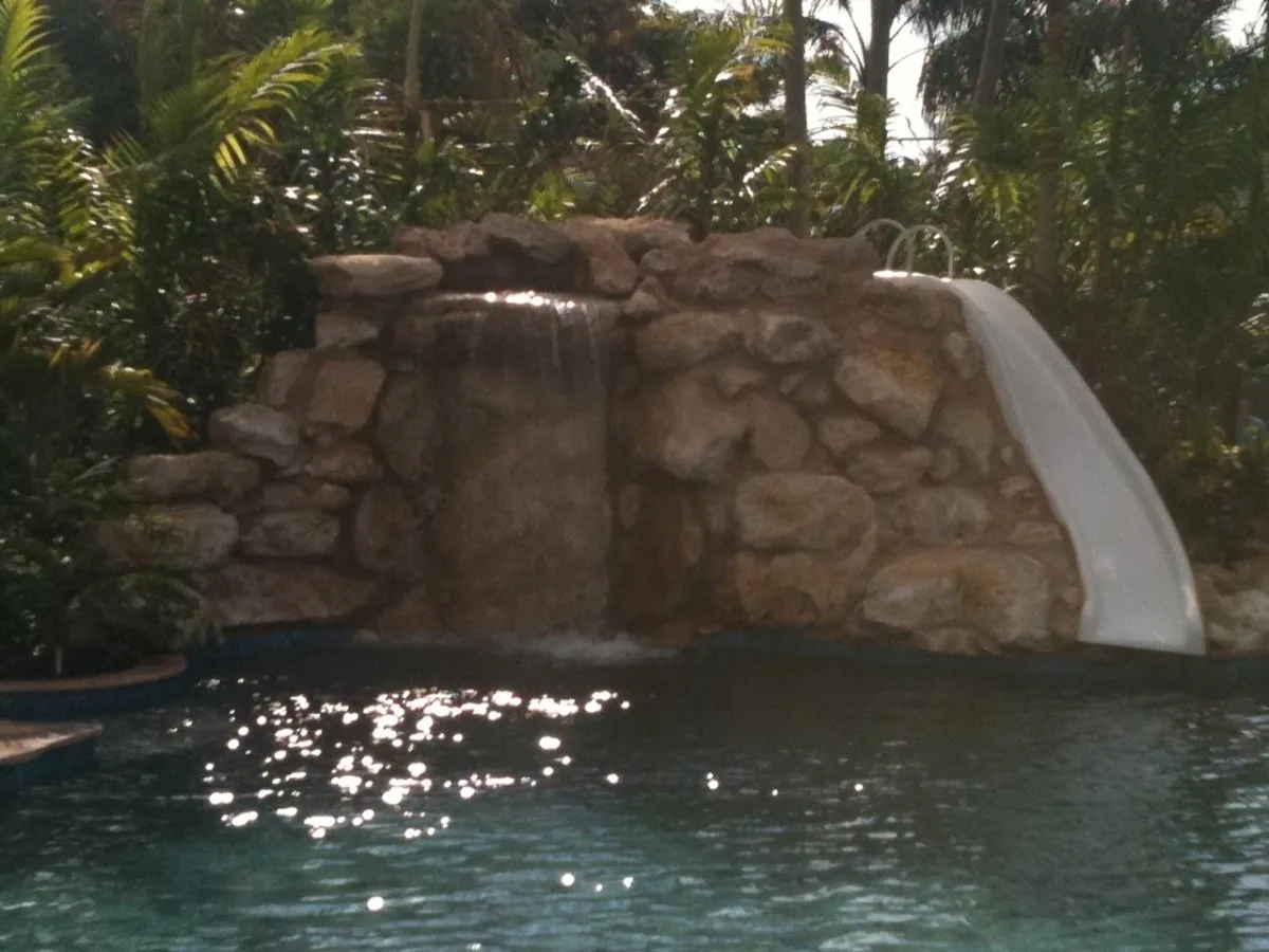 Rock waterfall and slide feature on a backyard swimming pool